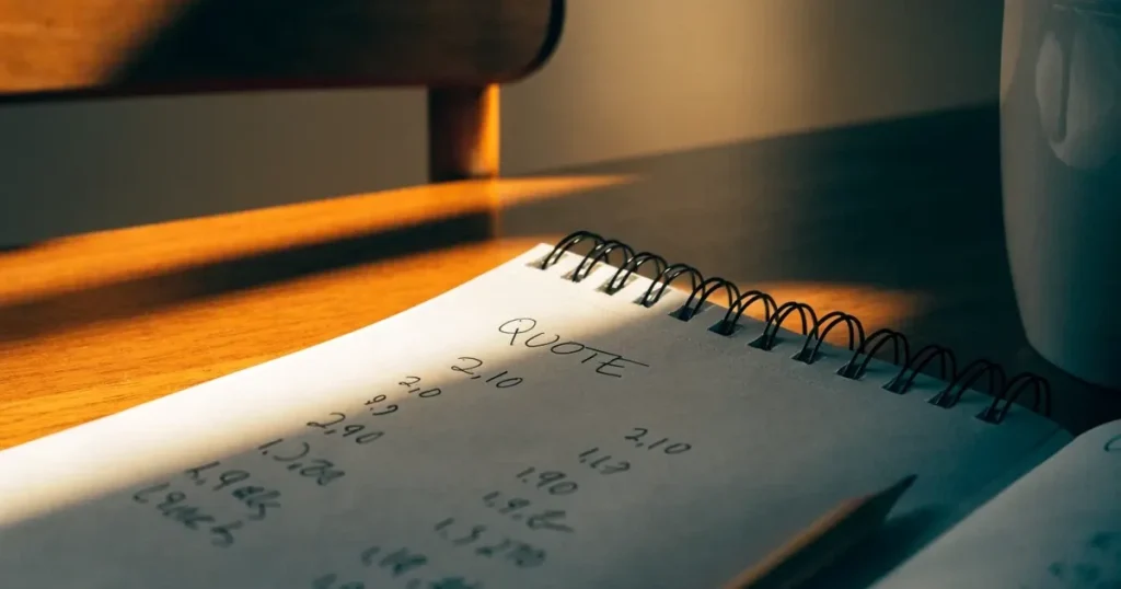 Un quaderno aperto con quote scritte a mano, una calcolatrice e una matita su un tavolo di legno